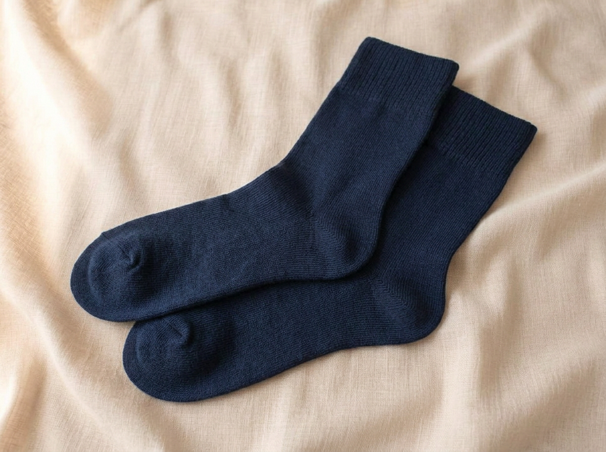 A pair of navy Kilde mercerized cotton socks resting softly on beige linen, one overlapping the other, showing the shaped heel pocket